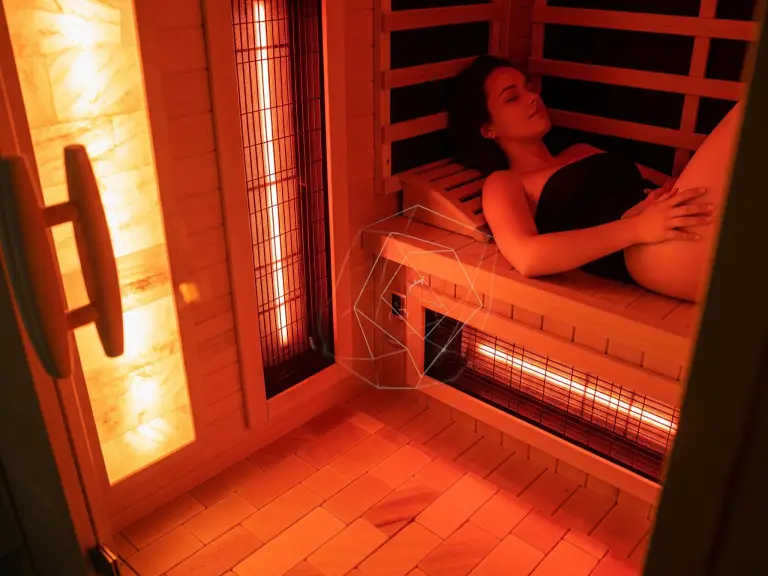 Inside a luxurious infrared home sauna with a Himalayan salt wall and subtle red light glow, showing a person experiencing deep relaxation and wellness benefits.